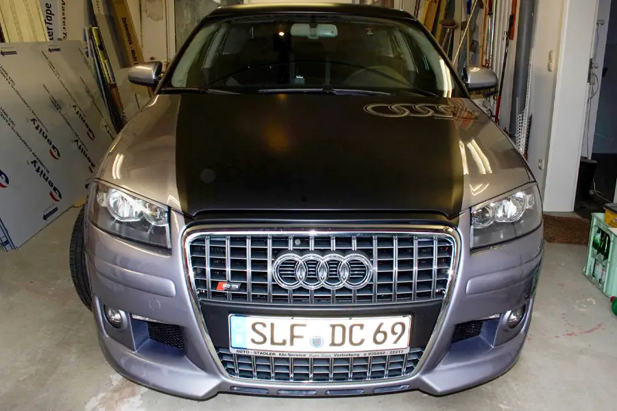 Vorderansicht eines grauen Audi S3 mit schwarzer Motorhaube, geparkt in einer Garage.